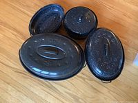 Three lids for oval roasting pans arranged on wood floor.