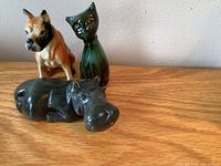 Front view of a large soapstone hippo lying down, with three smaller ceramic animals behind: a dog, a green cat, and a bulldog.