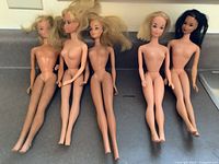 Five vintage Barbie dolls nude with blonde and black hair on a counter surface.