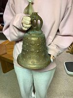 Front side of vintage brass bell showing the 1964 date and floral embossments.