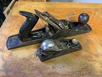 Two vintage woodworking hand planes on wooden surface, showing condition details and size difference