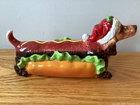 Side angled view showing dachshund shaped biscuit holder with hot dog and lettuce details and Santa hat on dog head