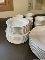 White ceramic cups and stacked saucers with large and smaller plates visible.