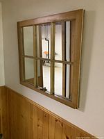 Frontal angle of the vintage window sash mirror mounted on a wall with wooden paneling below, showing six glass panels in a wooden frame.