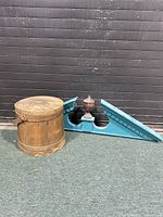 Wooden firkin with flat lid next to blue painted architectural trim with finial against black wall