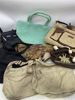 Overview of the grouping of seven used women's bags including the light blue woven tote, beige canvas bag, black nylon crossbody, brown and beige straw handbag, floral tapestry bag, and black mesh bag.