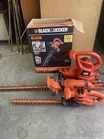 Black & Decker electric blower with original box and two hedge trimmers placed on a concrete floor.