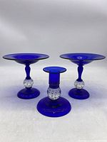 Front view of two blue glass compotes and one candlestick holder showing bubble details on stems.