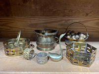 Overview of the grouping of brass items including baskets, napkin rings, swan figurine and bowl with brass balls.