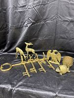 Overview of all brass decorative items on black cloth backdrop including wall hanging key, deer, eagle bookend, fish, and candle holder