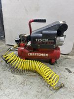 Side view of Craftsman air compressor showing label with specifications, red tank, black motor housing, and yellow coiled hose