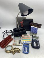 Overview photo showing all items in the lot: calculators, black desk lamp, pens, journals, paperweight, and notepad