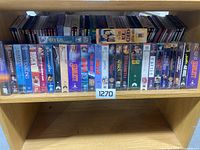 Shelf filled with various sealed DVDs and VHS movies, showing all items in the lot horizontally arranged.