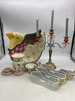 View of ornate Fitz & Floyd bird-shaped chip bowl, candelabra, porcelain bowl, and white flatware caddies with gold handles
