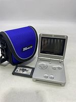 Silver Game Boy Advance SP handheld console open with screen and controls visible, blue carry case, and Kingdom Hearts: Chain of Memories game cartridge placed in front