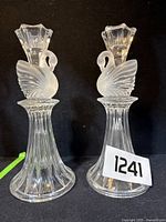Pair of glass swan candle sticks photographed against a black background with lot number tag visible