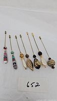 Seven stick and hat pins arranged side by side showing various decorative heads including patterned, faux pearl, and filigree designs.