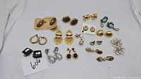 Overview of all 13 pairs of vintage earrings in various materials and styles arranged on white fabric.