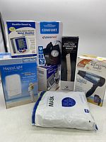 Wide view showing all boxed items including blood pressure monitors, UV sterilizer, hair dryer, and masks.