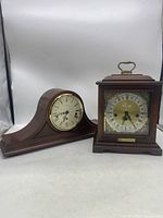 Photo showing both clocks side by side on white background, tambour style on left, square carriage style on right