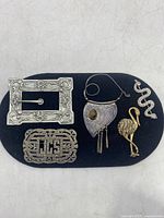Full lot of six pins and brooches displayed on a black felt background showing various shapes and materials including sterling silver and gold-tone.