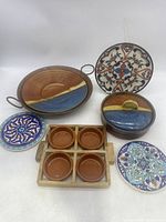 Overview of all items including large pottery dish in copper pot, four small terracotta dishes in wooden tray, and four decorated ceramic hot plates with hanging string on one.