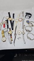 Image of a collection of 18 assorted wristwatches in various band materials and colors arranged on white background.