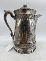 Front side view of the silver plated pitcher showing detailed maritime engraving and ornate handle.
