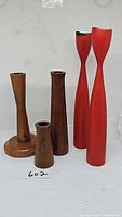 Grouping of five vintage Mid-Century Modern wood candlesticks, three in natural wood finish varying in height and two taller red painted wooden candlesticks with slim elongated shapes.