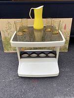 Front view of the plastic bar table with four amber glasses and a yellow enamel pitcher on top