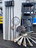 Four black metal tiki torch posts, metal tree sculpture, small patio side table, and garden decor pieces arranged vertically and on the ground in an outdoor setting.