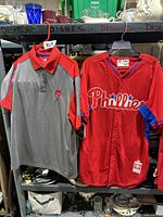 Red Philadelphia Phillies signed game jersey and gray and red dry fit polo shirt hanging from rack