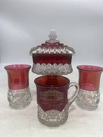 Front view of the ruby red glass compote candy dish with lid and three matching glasses arranged around it.