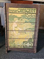 Front view of vertical wooden slat advertising board featuring American Crescent Cycles logo and vintage illustration of a woman with flowing hair in natural colors.