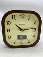 Front view of the clock showing the full face with numerals, brand name, and date/day display.