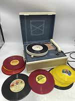 Photo showing Sears brand vintage child’s record player with several colorful 45 RPM children's records in red, yellow and black vinyl showing wear.