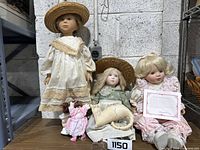 Image of set of four dolls on table including three porcelain and one small stuffed doll