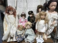 Wide view of 8 vintage porcelain dolls varying in size, hair color, and clothing style. Six come with stands. Visible wear and age consistent with vintage condition.