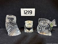 Front view of the three Waterford crystal animal figurines including owl, pig, and fish on black background.