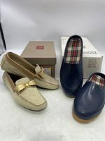Beige suede moccasin loafers and navy blue slip-on clogs with their original boxes in the background.