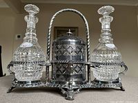 Front view of the antique crystal decanter set in silver plated stand with biscuit holder. Shows detailed cut glass design on decanters and ornate silver plating with handle and feet.