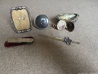 Top front view of six vintage desk accessories on grey fabric background showing frames, dish, locket, letter opener, and pocket tool.
