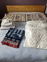 Photo showing large floral comforter, white quilted comforter, three pillows, and several towels including patterned beach towels.