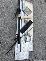 Overview of assorted metal parts laid on pavement including perforated panels, black rods, mesh, plate, and wire.