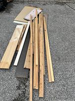 Various long wooden planks laid on ground alongside plywood and particleboard pieces.