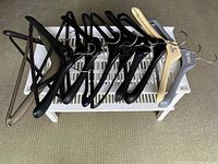 Photo of white plastic shelf with assorted coat hangers laid on top, showing eight black, one beige wooden, and one gray hangers.