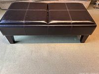 Front angled view of dark brown faux leather ottoman with visible stitching and panel divisions.