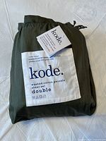 Folded dark olive green bedsheet set in packaging with Kode brand label showing 100% cotton washed percale double size sheet set