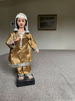 Front view of the Indian cultural figurine showing traditional attire in faded green/gold fabric with silver trim and a white head veil.