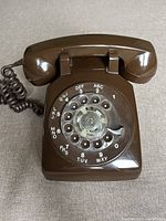 Top-down view of vintage brown rotary telephone showing circular dial with numbers and original handset with coiled cord.